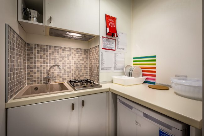 Cucina compatta con lavello, piano cottura, frigo e mosaico alle spalle.