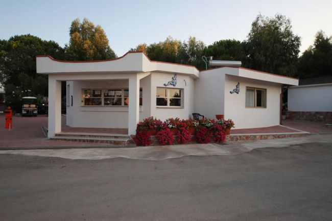 Edificio bianco con fiori rossi davanti, circondato da alberi.