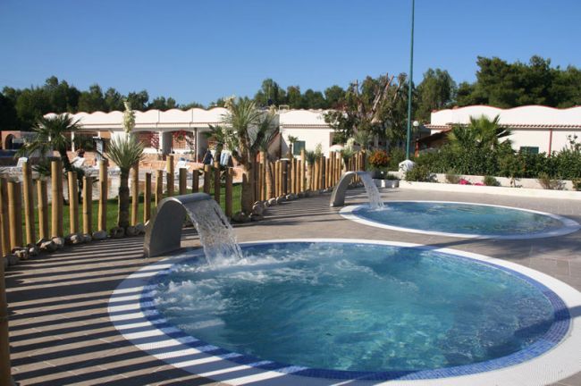 Due piscine circolari con cascate d'acqua in un giardino recintato da pali di legno.