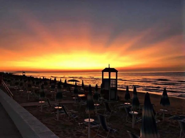 Spiaggia al tramonto con ombrelloni chiusi e mare calmo.