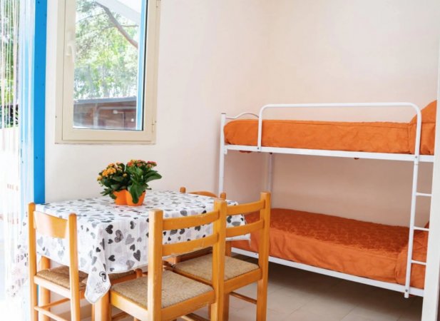 Interno con tavolo apparecchiato e letti a castello con coperte arancioni.