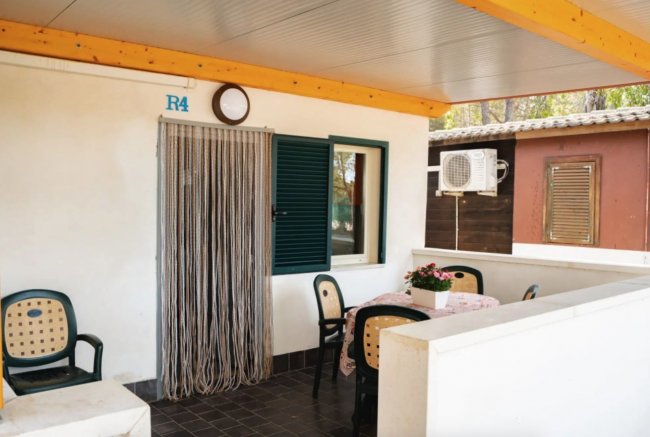 Portico con sedie, tavolo e piante. Tenda di corde sulla porta.