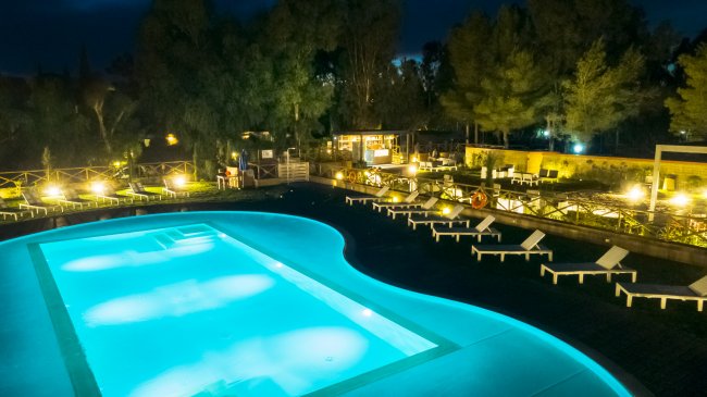 Piscina illuminata di notte, circondata da lettini.