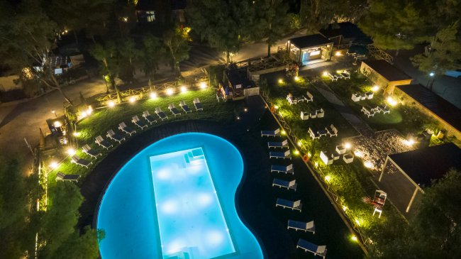 Piscina illuminata di sera con lettini e giardino.