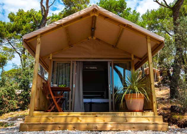 Tenda glamping con veranda e tavolo in legno.
