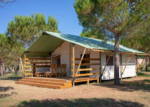 Tenda glamping con veranda in un campo alberato.