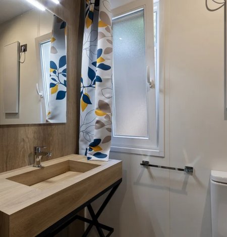 Bagno moderno con lavandino in legno e tende floreali.