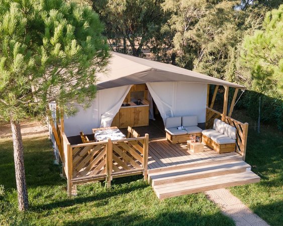Tenda glamping con veranda in legno in un'area verde.