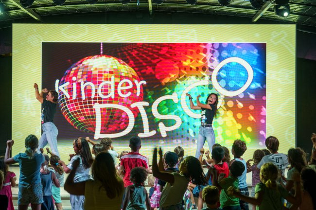 Bambini che ballano su un palco illuminato con scritta 