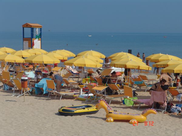 Spiaggia affollata con ombrelloni gialli e persone in relax.