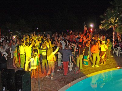 Festa serale all'aperto con molte persone che ballano accanto a una piscina.