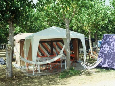 Un'area campeggio con una tenda grande, circondata da alberi e sedie a sdraio.