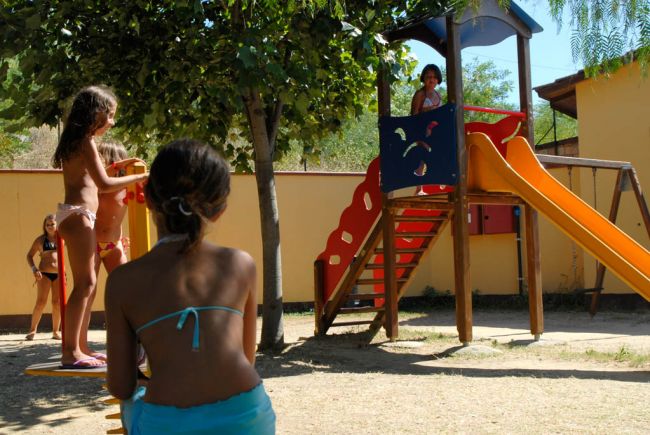 Parco giochi con scivolo arancione e bimbi che giocano.