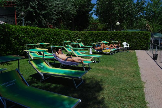 Persone che prendono il sole su sdraio verdi in un prato accanto alla piscina.