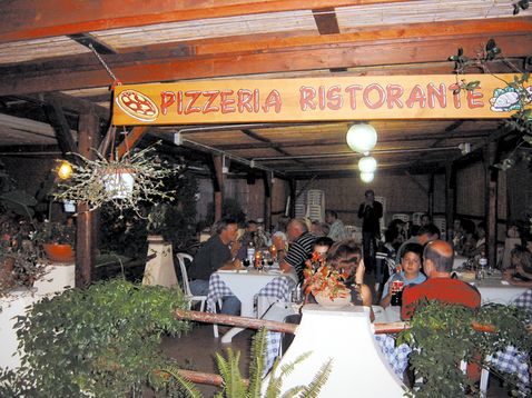 Ristorante pizzeria all'aperto con tavoli occupati da clienti.