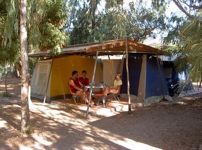 Tenda da campeggio tra gli alberi con tre persone sedute.