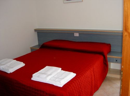 Letto matrimoniale con copriletto rosso acceso, due asciugamani piegati sui piedi del letto.