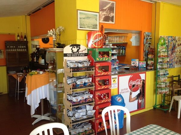Interno di un negozio colorato con scaffali di snack e bibite, sedie e tavoli.