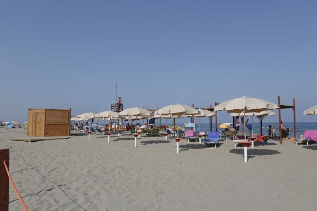 Ombrelloni e lettini sulla spiaggia sabbiosa, cielo sereno.