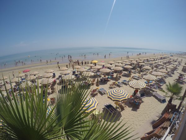 Spiaggia gremita con ombrelloni a strisce.