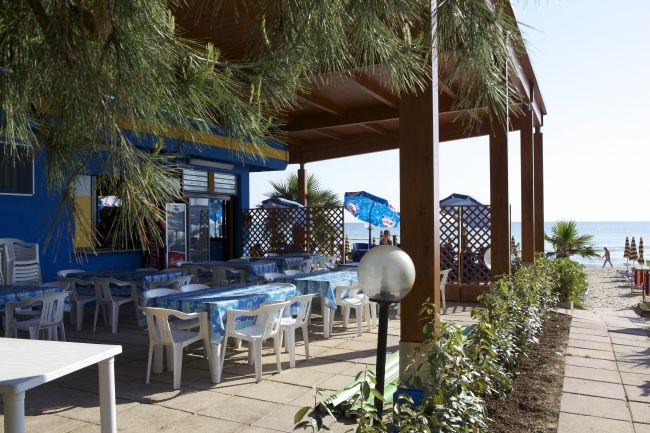 Ristorante all'aperto vicino al mare con tavoli e sedie bianche.