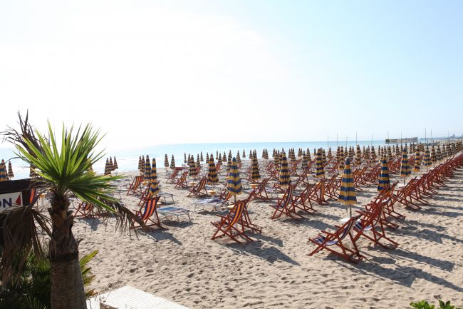 Spiaggia sabbiosa con lettini e ombrelloni colorati in fila.