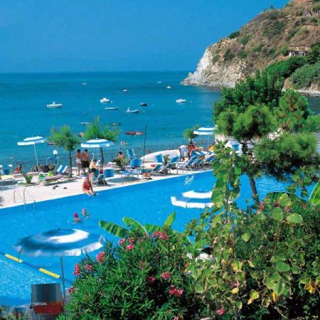 Piscina con vista mare, lettini e ombrelloni.
