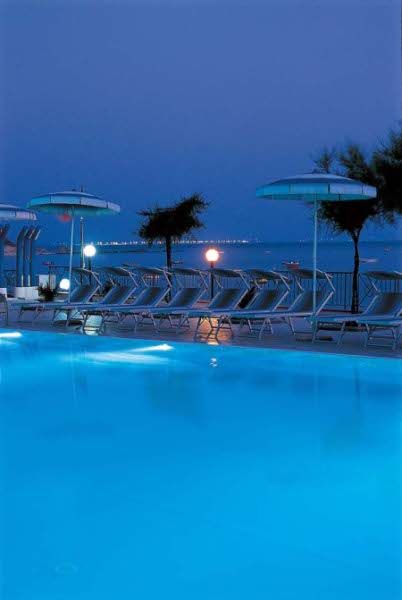 Piscina illuminata al crepuscolo con sdraio e ombrelloni.