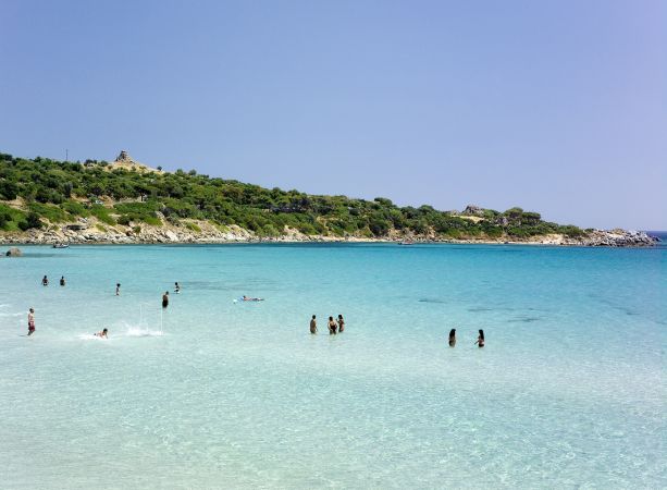 Persone che nuotano in mare limpido e azzurro vicino a una costa verde.
