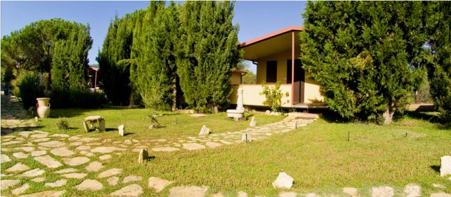 Un giardino ben curato con viali in pietra e una piccola struttura gialla tra gli alberi.