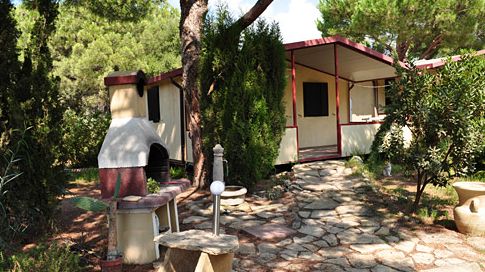Un bungalow immerso nel verde con un caminetto esterno e un sentiero lastricato.