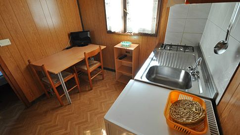 Cucina compatta con lavandino, fornelli, tavolo e sedie, illuminata da una finestra.