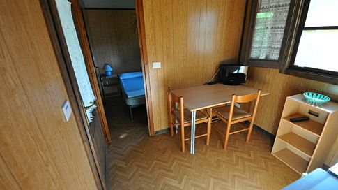 Interno di una stanza con tavolo, due sedie, scaffale e letto in una camera adiacente.