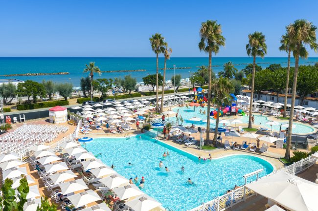 Piscina all'aperto con ombrelloni e palme.