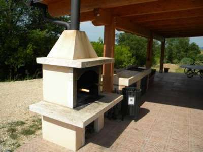 Un barbecue in pietra sotto un tetto di legno, con uno spazio esterno lastricato.