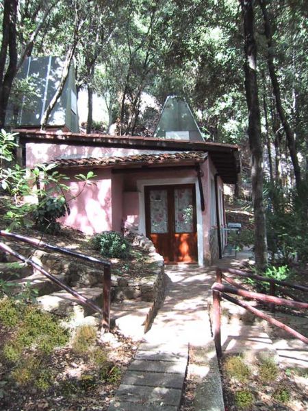Una piccola casa rosa tra alberi con sentiero in pietra.