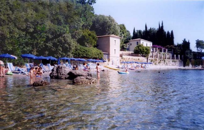 Spiaggia con ombrelloni blu, persone in acqua e edifici sullo sfondo.