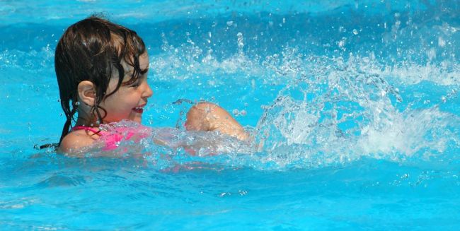 Bambina che gioca e sorride in una piscina, spruzzando acqua.