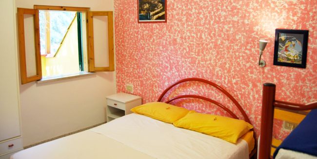 Camera da letto con pareti rosa, letto matrimoniale, e finestrella aperta.
