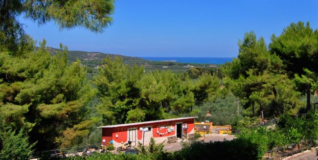 Una casetta rossa immersa nel verde con vista sul mare in lontananza.