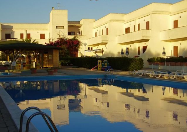 Complesso residenziale con piscina e sdraio.