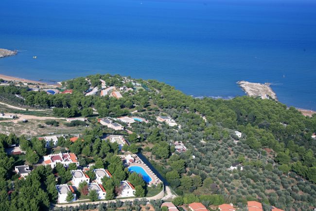 Vista aerea di una località costiera con piscine e vegetazione rigogliosa.