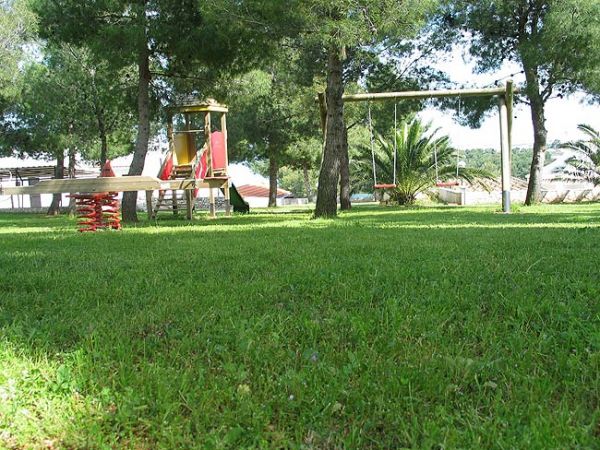 Prato con altalena e giochi sotto gli alberi.