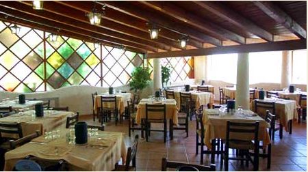 Sala ristorante con tavoli apparecchiati e parete con vetri colorati.