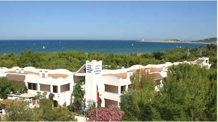 Vista di un edificio bianco immerso nel verde con il mare sullo sfondo.