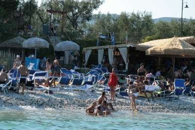 Spiaggia affollata con sdraio blu, ombrelloni di paglia e persone in relax.