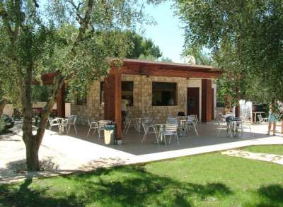 Un bar in pietra con terrazza all'aperto, circondato da prato verde e alberi.