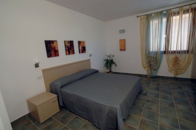 Una camera da letto con letto matrimoniale, piastrelle verdi e finestre con tende leggere.