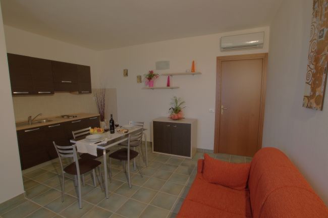 Soggiorno con cucina, tavolo apparecchiato e divano arancione.