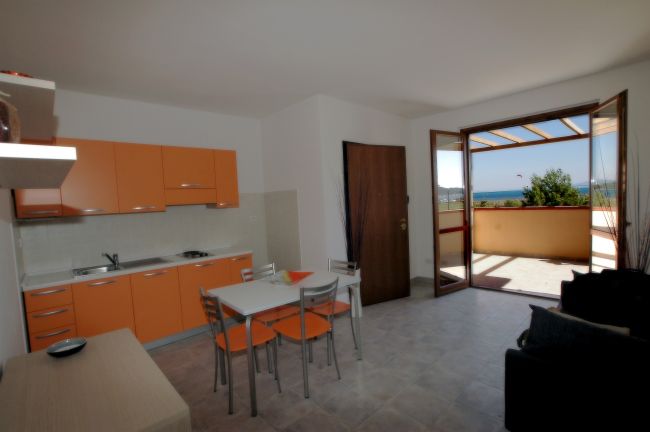 Cucina moderna arancione, tavolo e sedie, porta aperta su terrazza con vista.